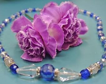 May include: A purple and white flower necklace with blue and clear glass beads.