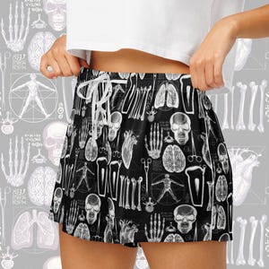 Op de afbeelding: Zwarte sport shorts met een witte anatomische print. De print bevat botten, organen en schedels.