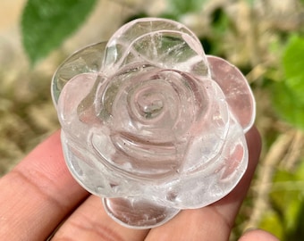 May include: A clear quartz crystal carved into the shape of a rose. The rose is detailed with delicate petals and a center swirl.