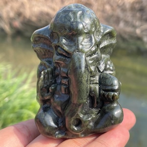 Op de afbeelding: Een klein, donkergroen, gesneden stenen beeldje van de hindoe-god Ganesha. Het beeldje is gedetailleerd en toont Ganesha zittend met zijn slurf omhoog en zijn handen in een gebedspositie.