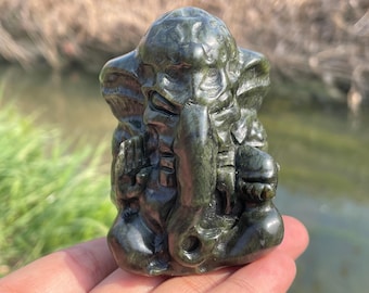 Puede incluir: Una pequeña escultura de piedra de color verde oscuro tallada de la deidad hindú Ganesha. La escultura es detallada y muestra a Ganesha sentado con la trompa levantada y las manos en posición de oración.