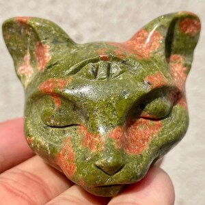 May include: Green and red speckled stone cat sculpture with a third eye in the center of its forehead.
