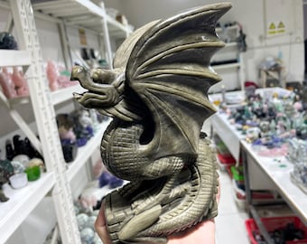 Puede incluir: Una escultura de dragón de jade verde con detalles intrincados. El dragón está enroscado con las alas extendidas. La escultura está hecha de una piedra lisa y pulida.