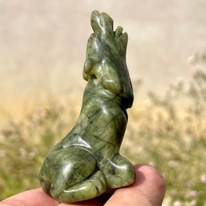 Puede incluir: Talla de jade verde de un perro sentado con la cabeza levantada. La talla es detallada y realista.