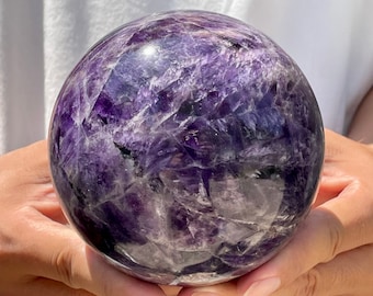 May include: A large, polished amethyst sphere with a deep purple color and white inclusions. The sphere is smooth and has a high gloss finish.