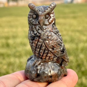 Könnte beinhalten: Eine geschnitzte Eulenfigur aus schwarzem und rotem Jaspis. Die Eule sitzt auf einem runden Sockel und hat komplizierte Details.