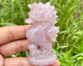 May include: A pink rose quartz seahorse figurine. The seahorse is carved with intricate details and has a smooth, polished finish.