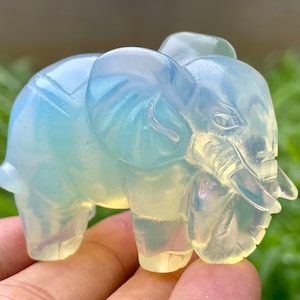 May include: A small, translucent, light blue opal elephant figurine. The elephant is carved with detailed features, including its trunk, ears, and eyes.