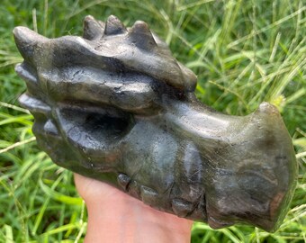 Puede incluir: Una escultura de cabeza de dragón tallada a mano en piedra de labradorita verde. La escultura tiene detalles intrincados, incluyendo dientes afilados y una superficie texturizada.