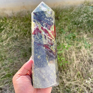 May include: A green, black and red crystal point with a pointed top and a flat base. The crystal has a swirling pattern of colours.