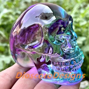 May include: A crystal skull sculpture with iridescent purple, blue, and green colors. The skull is made of clear glass and has a smooth, polished finish.