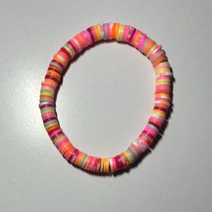 May include: A colorful bracelet made of small, round, flat beads in shades of pink, orange, yellow, and white.
