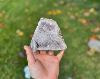Könnte beinhalten: Ein großer Amethyst-Kristall-Cluster in violetter und weißer Farbe. Der Kristall hat die Form einer Pyramide und eine raue, natürliche Textur.