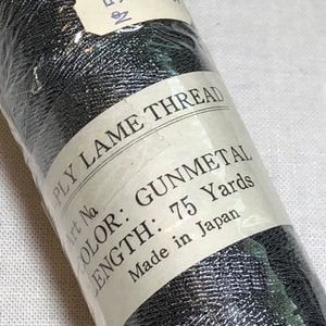 May include: A spool of gunmetal colored lame thread, 75 yards long, made in Japan. The label reads "PLY LAME THREAD", "COLOR: GUNMETAL", "LENGTH: 75 Yards", "Made in Japan", and "N5886".