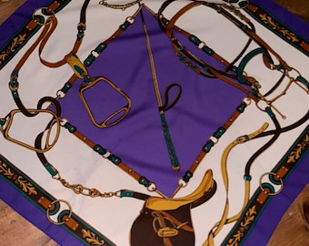 Può includere: Un foulard di seta viola con sfondo bianco e un disegno di equipaggiamento equestre marrone, oro e verde, tra cui una sella, staffe e redini.