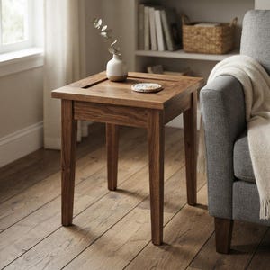May include: A square wooden side table with four straight legs and a natural wood grain finish. On the tabletop sits a small, off-white ceramic vase containing a single sprig of greenery and a round, textured coaster with a speckled pattern.