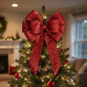 May include: A large, glittery red bow tree topper sits atop a green Christmas tree. The bow features wide, textured loops and two long, hanging tails. The tree is decorated with warm white string lights, red and silver ornaments, and silver tinsel.