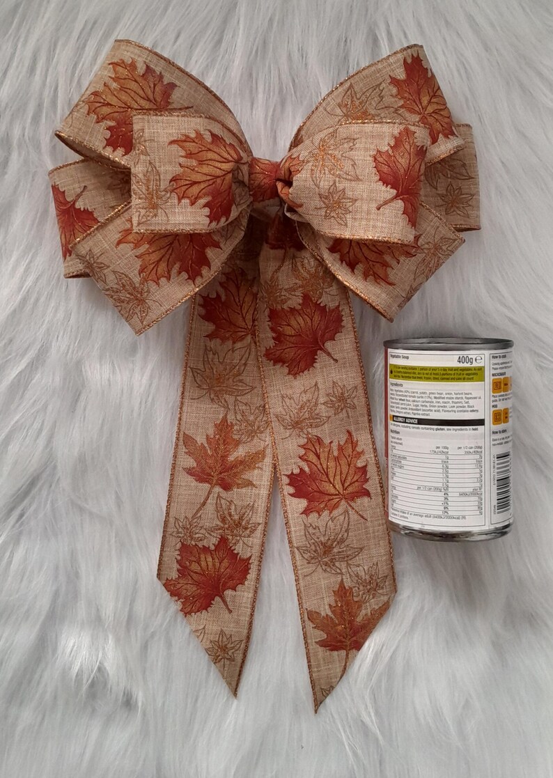 May include: A large decorative bow with a fall leaf pattern in shades of brown, orange, and red. The bow is made of fabric and has long streamers. A can of food is next to the bow.