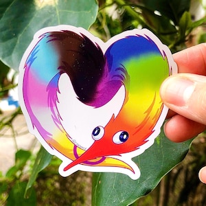Puede incluir: Un gusano de colores arcoíris con ojos grandes en forma de corazón. El gusano es rojo, naranja, amarillo, verde, azul, morado y negro. El gusano está sosteniendo un anillo en su boca. El texto "@Leccaart" es visible en la pegatina.