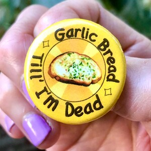 May include: Yellow button with the text "Garlic Bread 'Till I'm Dead" and a picture of a slice of garlic bread.