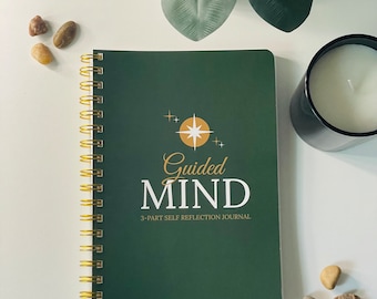 May include: A green spiral bound journal with the words "Guided Mind" and "3-Part Self Reflection Journal" printed in white and gold. The cover features a gold star with a white outline.
