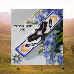 May include: A white beaded bracelet with a black and gold geometric design. The bracelet has blue and gold accents and the text "Out of the Flames 2013" is visible.