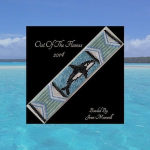 May include: A beaded bracelet with a black and white orca whale design on a blue background. The bracelet is surrounded by a black border and the text "Out Of The Flames 2014" is at the top. The text "Beaded By Joan Maxwell" is at the bottom.