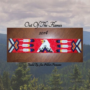 May include: A beaded Native American style bracelet with a red background, white eagle design, and blue and yellow accents. The bracelet is on a wooden surface and the text "Out Of The Flames 2014 Beaded By Jan Hebert Parmenter" is below the bracelet.