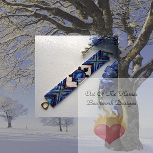 May include: A white, blue, and gold beaded bracelet with a geometric pattern. The bracelet is on a white surface with a blurred background of a snowy landscape and a tree.