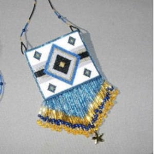 Pode incluir: Um colar de contas com uma bolsa branca com um design geométrico e franjas azuis. A bolsa tem uma faixa preta e branca e um amuleto de estrela dourada.
