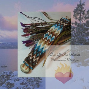 May include: A beaded bracelet with a brown, white, and blue geometric pattern. The bracelet has a bone-like clasp and is accented with gold beads. The bracelet is displayed on a background of brown branches and a blurred image of a snowy landscape. The text "Out Of The Flames Beadwork Designs" is visible in the image.