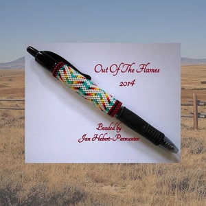 May include: A black pen with a beaded barrel featuring a colorful geometric pattern in white, turquoise, yellow, and red. The pen is labeled "Out Of The Flames 2014" and "Beaded by Jan Hebert-Parmenter".