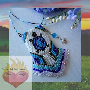 Könnte beinhalten: Handgefertigte Perlenanhänger-Halskette mit einem Schildkröten-Design. Der Anhänger ist weiß mit einer blauen Schildkröte, und die Fransen sind blau und weiß. Die Halskette enthält einen kleinen Schildkrötenanhänger und den Text "Out Of The Flames Bead Designs".