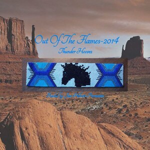 May include: A beaded bracelet with a black horse silhouette on a white background. The bracelet is blue, white, and light blue. The text "Out Of The Flames-2014" and "Thunder Hooves" is above the bracelet.