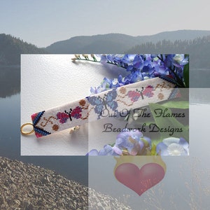 May include: White beaded bracelet with a design of pink and blue butterflies. The bracelet has a gold clasp and is made by Out of the Flames Beadwork Designs.