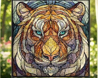 Könnte beinhalten: Buntglasfenster mit dem Gesicht eines Tigers in leuchtenden Orange-, Gelb- und Lilatönen. Der Tiger hat blaue Augen und einen schwarzen Rahmen. Das Wort "Name" steht unten. Das Fenster hängt vor einem Fenster.