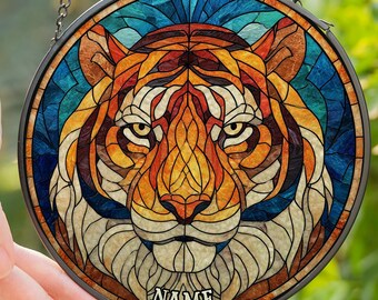 Könnte beinhalten: Runde Glasmalerei mit einem Tigergesicht. Das Design verwendet orange, gelbe, braune und blaue Glasteile. Die Tafel ist schwarz umrandet und an einer Kette aufgehängt. Das Wort "NAME" steht unten.