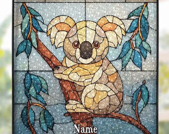 Könnte beinhalten: Buntglasfenster mit einem Koala, der auf einem Ast sitzt. Der Koala ist in Beige-, Braun- und Cremetönen gehalten, mit schwarzer Nase und Augen. Das Panel enthält blaue Blätter und das Wort "Name" am unteren Rand.
