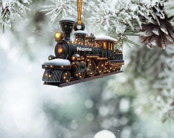 May include: A black and gold train ornament with lights and snow on top. The train has the word "Name" on the side.