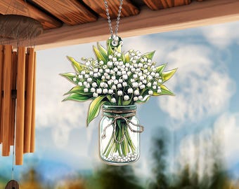 Könnte beinhalten: Ein weißer und grüner Blumenstrauß aus Maiglöckchen in einem durchsichtigen Glasgefäß mit einer braunen Kordelschleife. Der Strauß hängt an einer silbernen Kette.