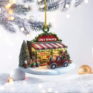 May include: A red and white Christmas ornament shaped like a small grocery store with a red truck in front. The store has a sign that says "Lily's Grocery".
