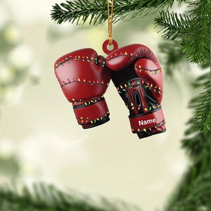 May include: Red boxing gloves with colorful lights strung around them. The gloves are hanging from a Christmas tree branch. The glove on the right has the word "Name" written on it.