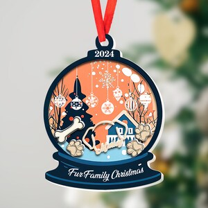 May include: A blue and white Christmas ornament with a snow globe design. The globe features a dog, a house, a Christmas tree, and the text "Fur Family Christmas". The ornament also includes the year "2024".
