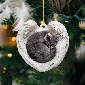 May include: White ceramic ornament shaped like a heart with angel wings. A gray cat is curled up inside the heart. The ornament has the word "Name" written on it.