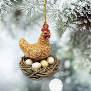 May include: A brown and white ceramic chicken ornament sitting in a woven nest with white eggs. The ornament is hanging from a gold string.