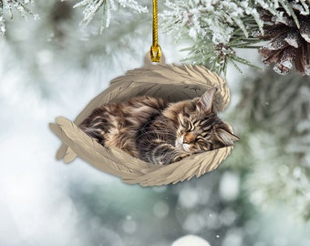 Könnte beinhalten: Ein brauner und weißer Katzenanhänger, der in einem Paar Engelsflügel schläft. Der Anhänger ist aus hellem braunen Material gefertigt und hat eine goldene Schnur zum Aufhängen.
