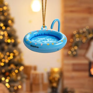 May include: A blue inflatable pool with a yellow spout and a floral pattern. The pool is hanging from a gold string and has the word "Name" printed on the side.