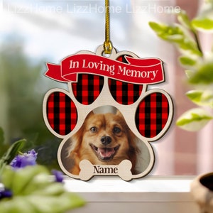May include: Wooden paw print ornament with a red and black buffalo plaid design. The ornament has a photo frame with a dog's face in it and the text "In Loving Memory" and "Name".