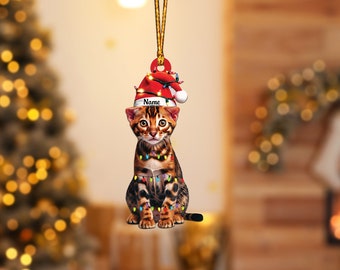 Könnte beinhalten: Ein Weihnachtsbaumschmuck mit einem süßen Kätzchen, das einen Weihnachtsmann-Hut trägt und in Weihnachtslichter verwickelt ist. Der Schmuck ist mit dem Namen "Name" personalisiert.