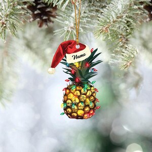 May include: A pineapple Christmas ornament with a red Santa hat and colorful lights. The ornament has the word "Name" written on it.